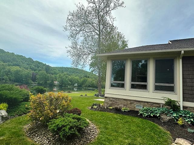River-side view of the cottage with the sunroom's bank of windows on the right, the Allegheny visible through trees on the left, a tall sycamore rising from the lawn, the ridge holding the far bank
