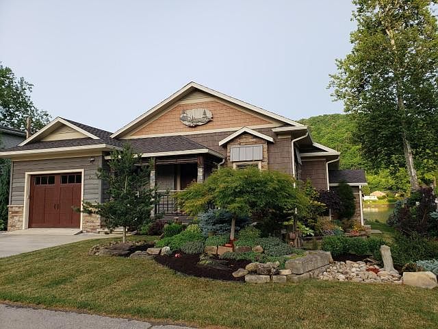 Front elevation of 2281 Dunns Eddy Rd, a custom Craftsman cottage with stone-pier facade, wood-shingle gables, and an attached garage tucked against a wooded Allegheny hillside